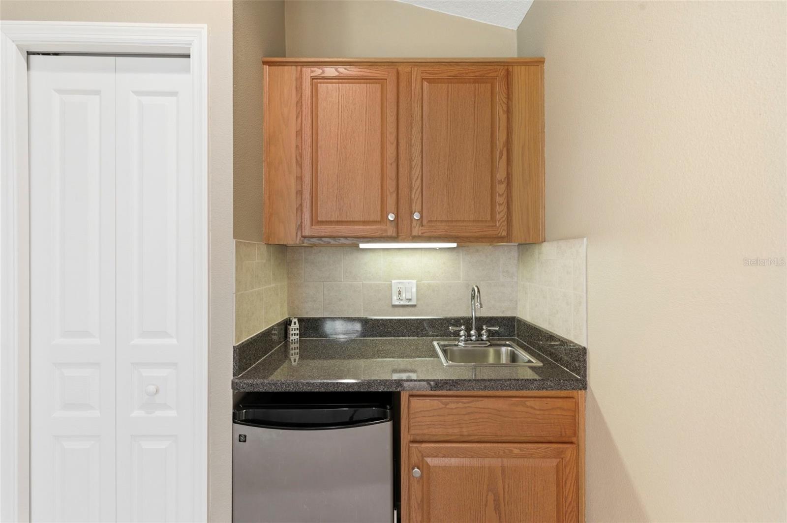 Convenient wet bar area featuring granite countertops, upper and lower cabinetry, and a built-in mini fridge—perfect for entertaining or creating a private refreshment station. Thoughtfully tucked away, this space adds both function and flexibility for hosting, relaxing, or everyday convenience.