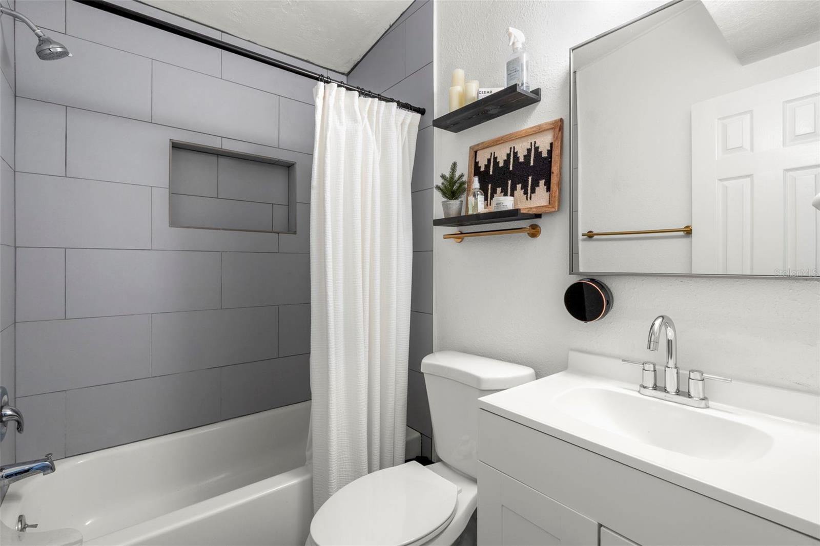 Updated bathroom with modern mirrored vanity with storage  and oversized tile surround.