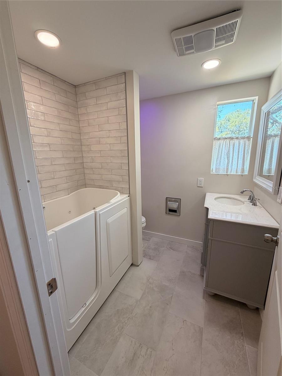 Remodeled bathroom with walk in bathtub and new tile, vanity and toilet.