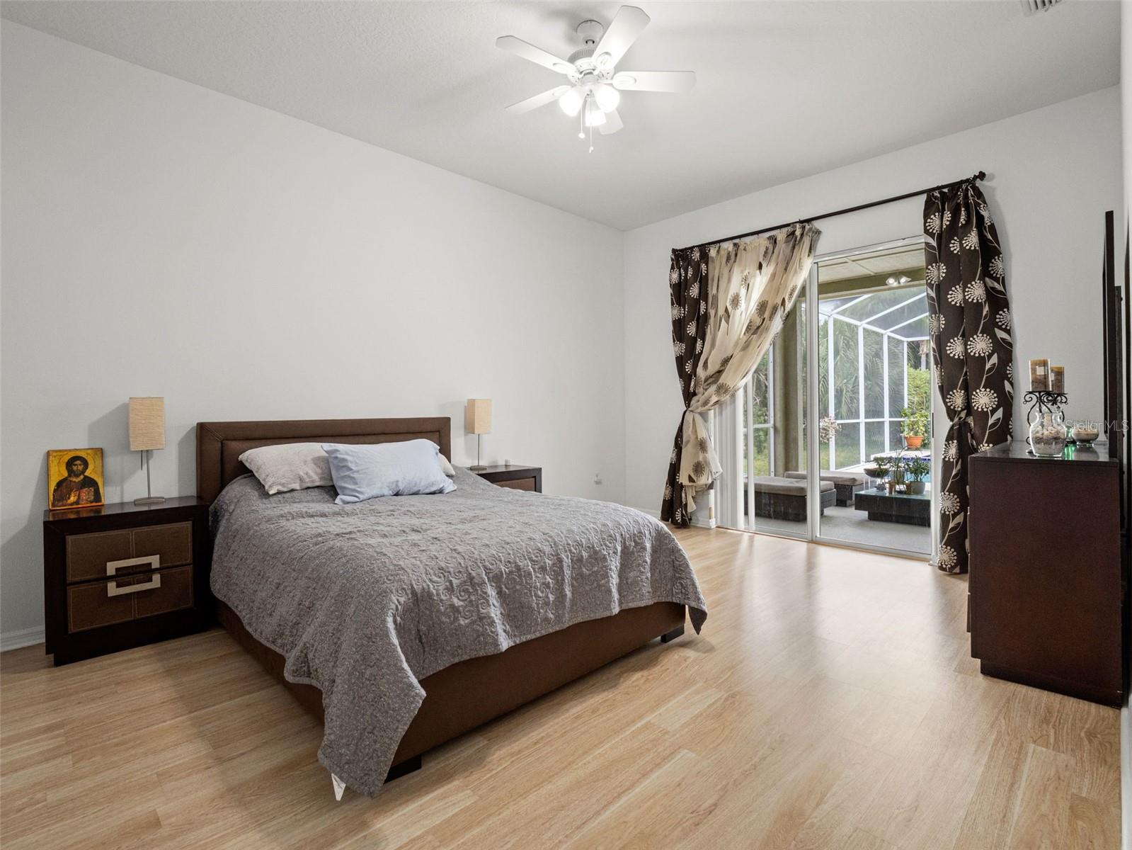 Spacious and light-filled primary suite featuring vaulted ceilings, wood-style flooring, and direct access to the covered lanai through sliding glass doors. A serene retreat with seamless indoor-outdoor flow.