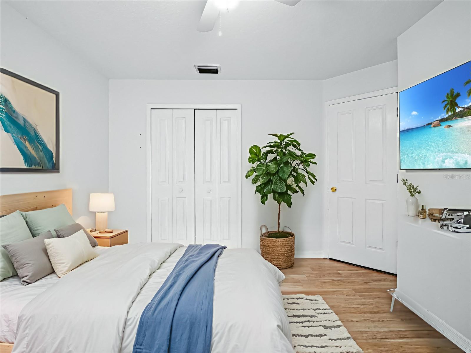 Bright and inviting bedroom featuring neutral tones, wood-look flooring, and a ceiling fan for added comfort, with ample natural light enhancing the space.