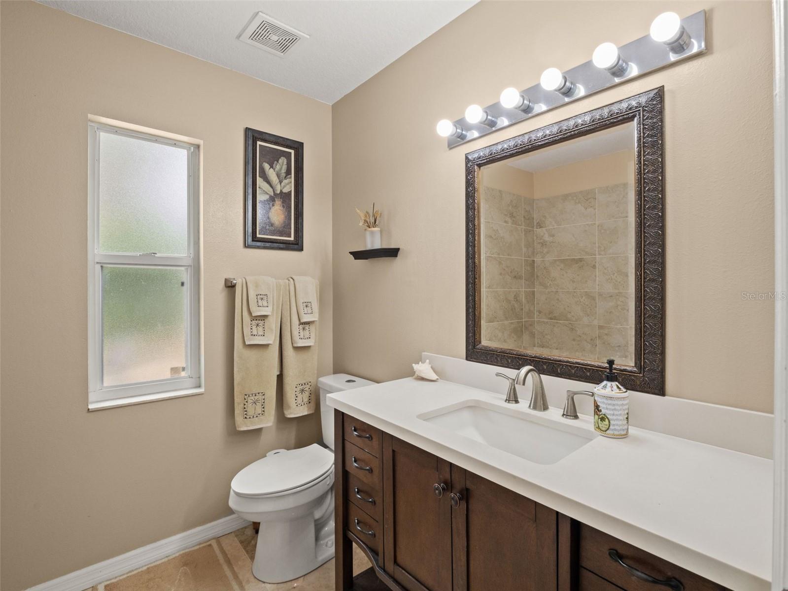 Stylish bathroom featuring a modern vanity with solid surface countertop, updated fixtures, and a framed mirror, complemented by natural light from the window.