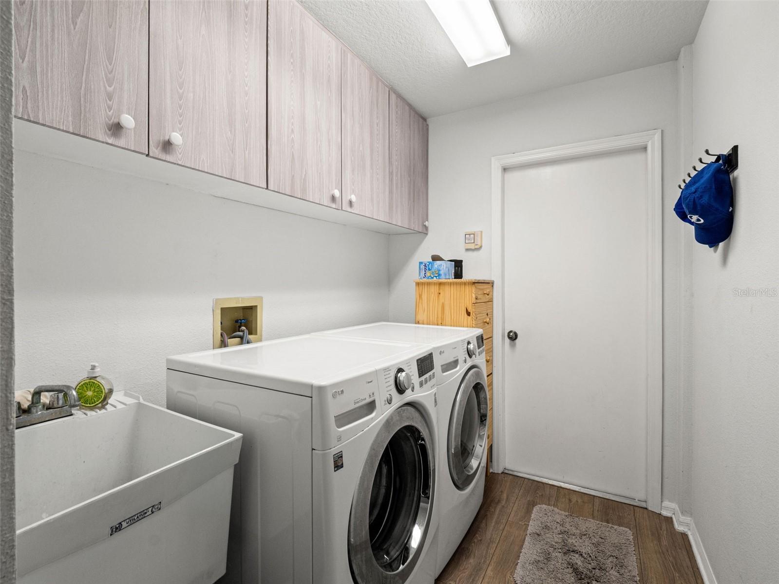 Dedicated laundry space with upper cabinetry for storage and a utility sink for added convenience.