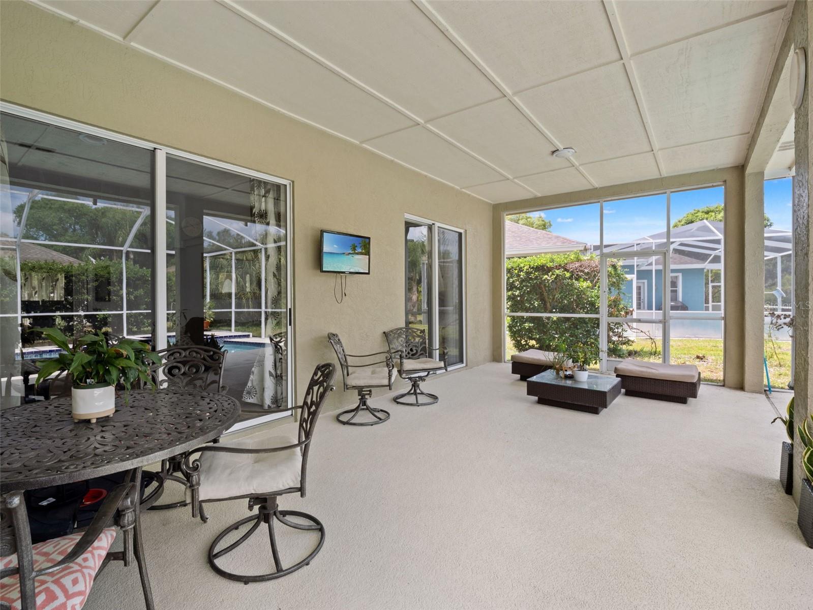 Spacious screened lanai with multiple seating areas, ideal for relaxing or entertaining while enjoying views of the pool and backyard.