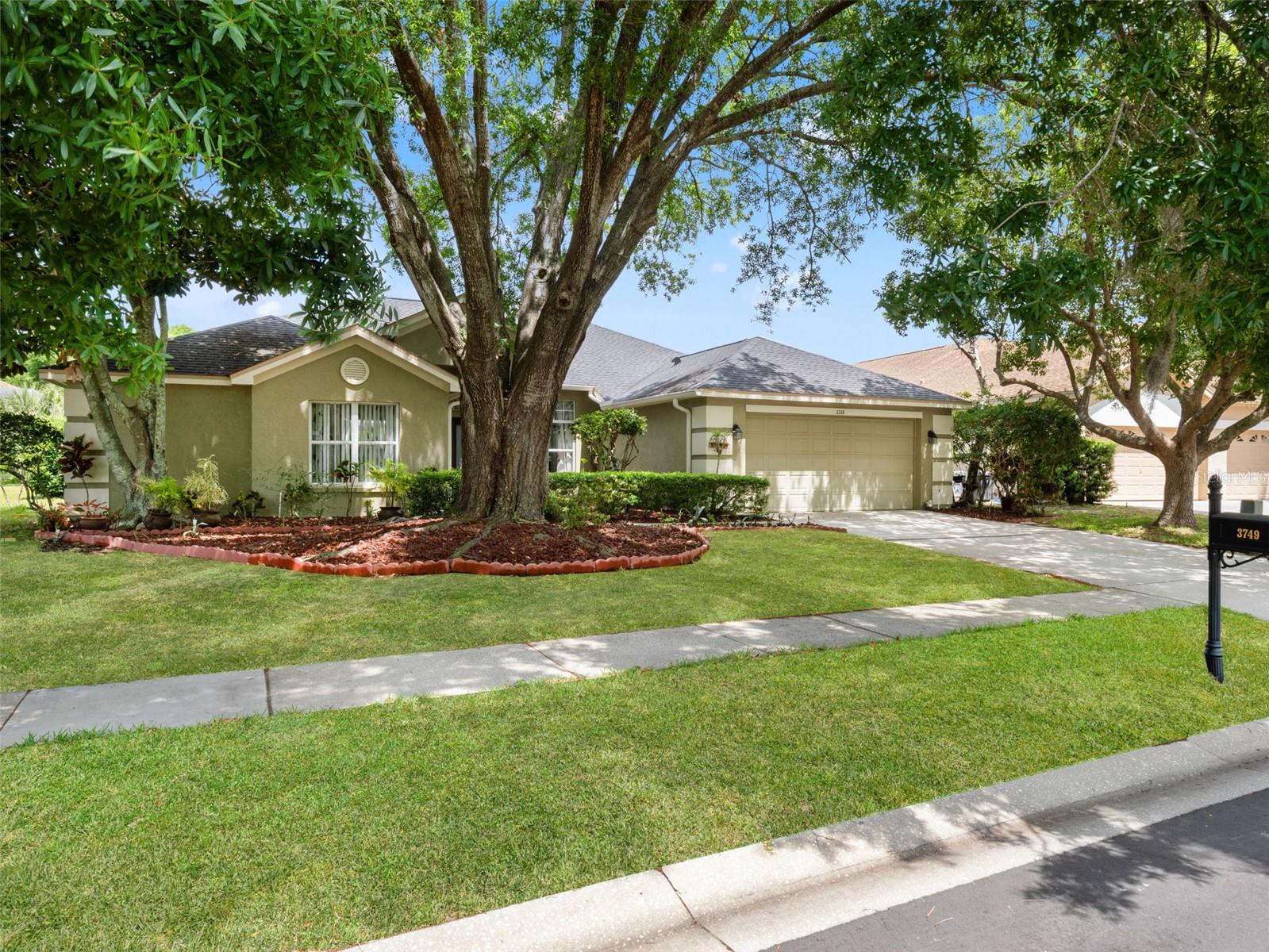 Charming front elevation with mature landscaping, shade trees, and a welcoming driveway leading to a two-car garage.