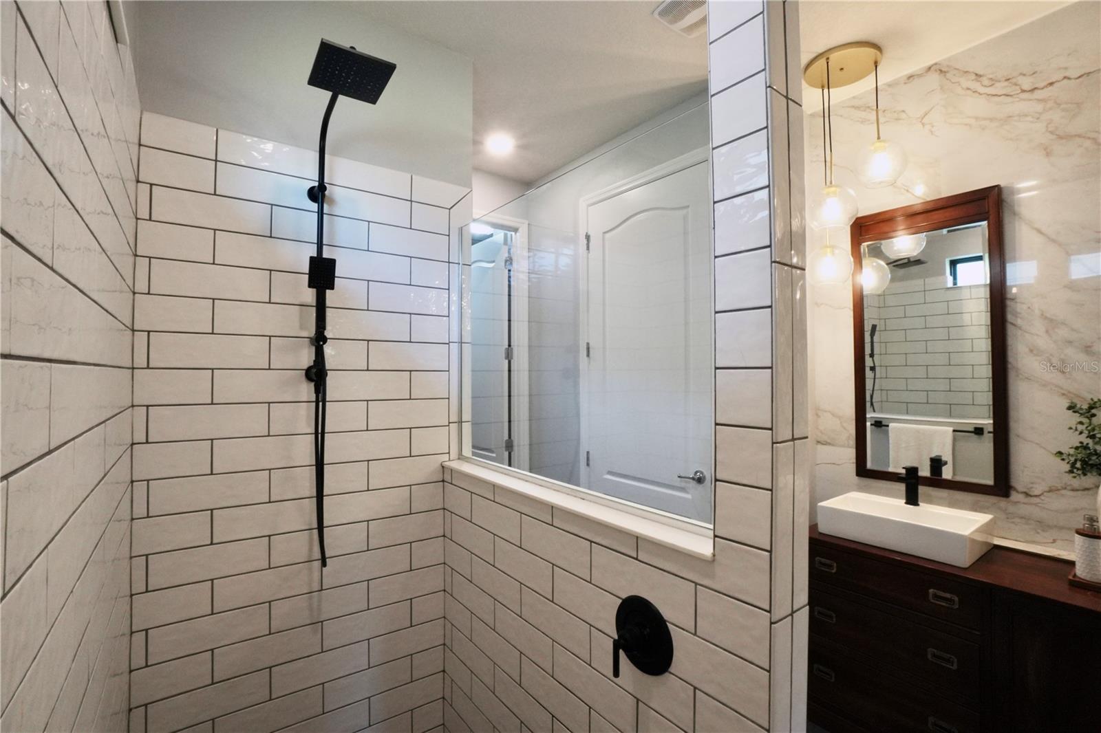 Upgraded shower head with faucet located near the entrance of the shower.