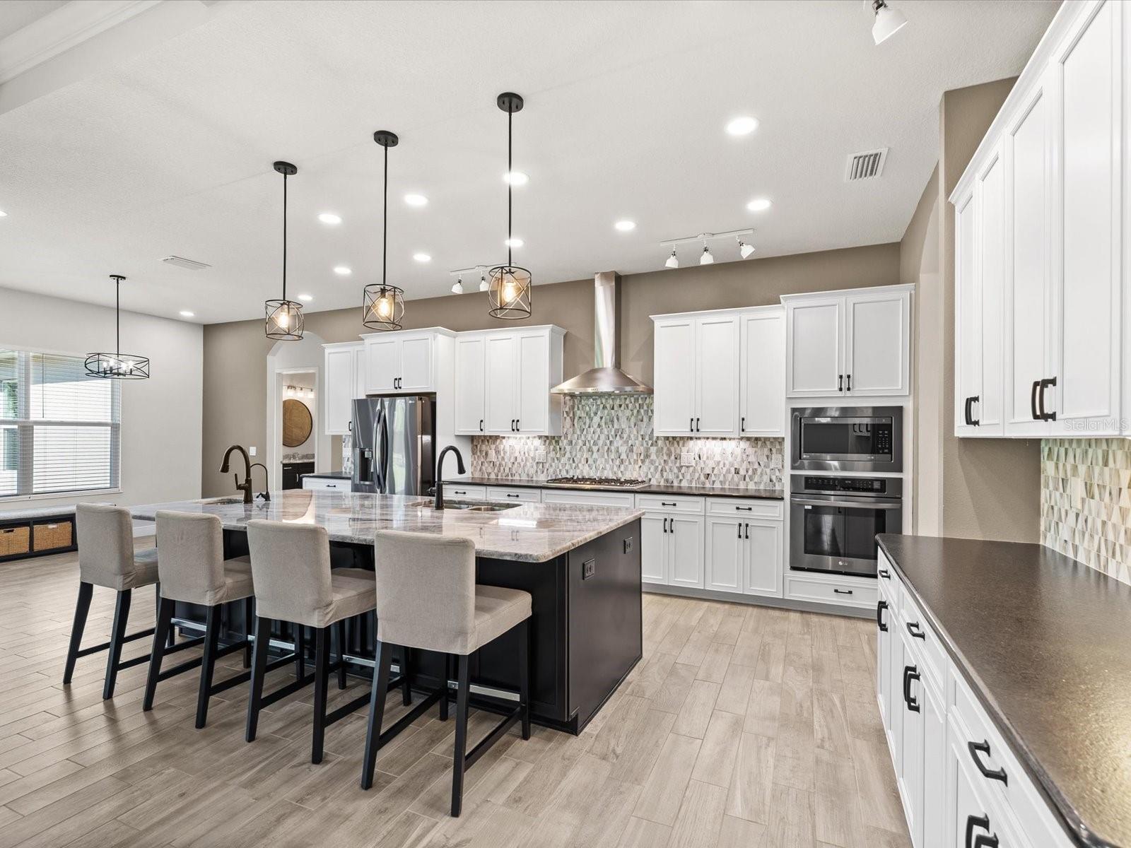 The stunning eat-in kitchen is the true centerpiece of the home, complete with an oversized granite island, Viking propane cooktop, built-in convection oven with microwave, and elegant high-end finishes.