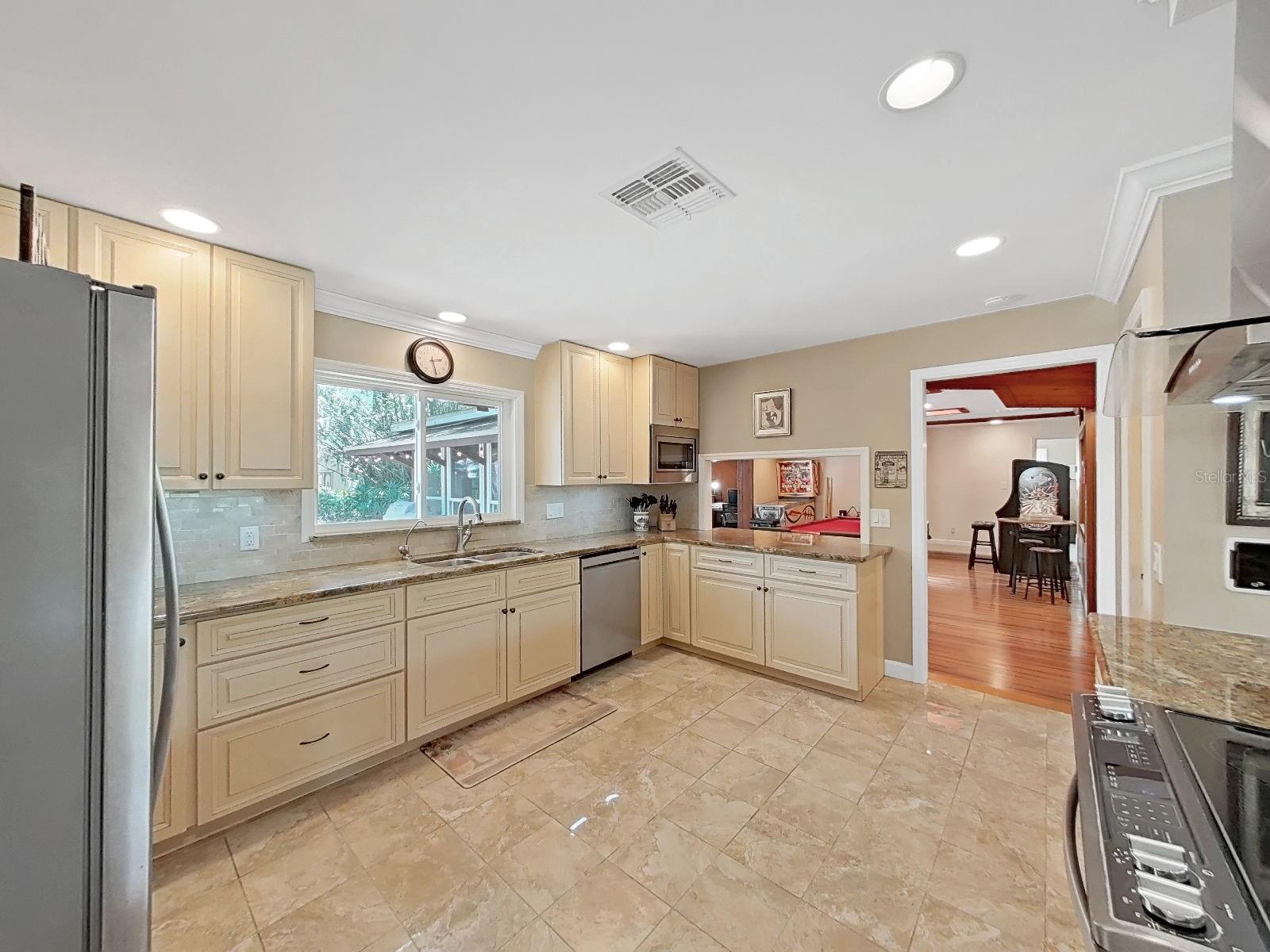 Bright, airy kitchen with light cabinetry, granite counters, undercabinet lighting, and open pass-through bar & view into the Bonus Game Room and beyond.