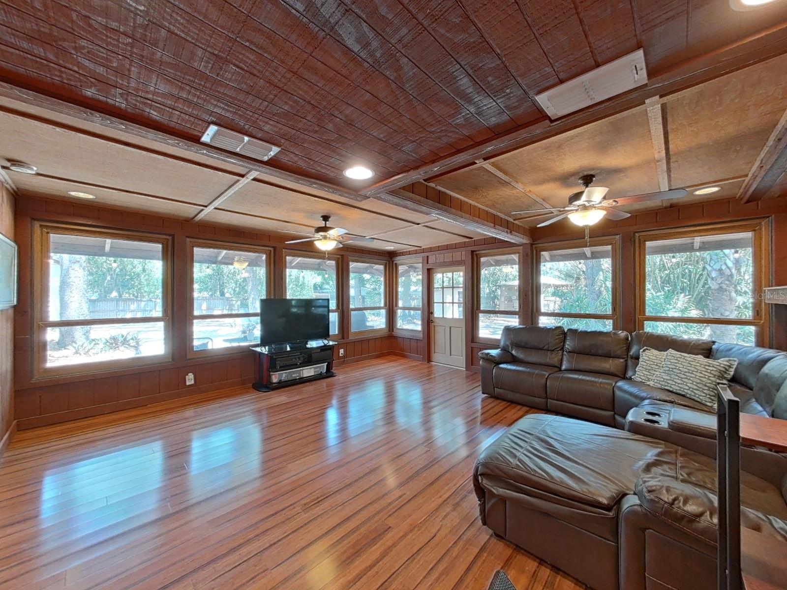 Expansive Florida Family Room with warm wood ceiling, gleaming wood floors, dual ceiling fans, & wraparound windows bringing the outdoors in year-round.