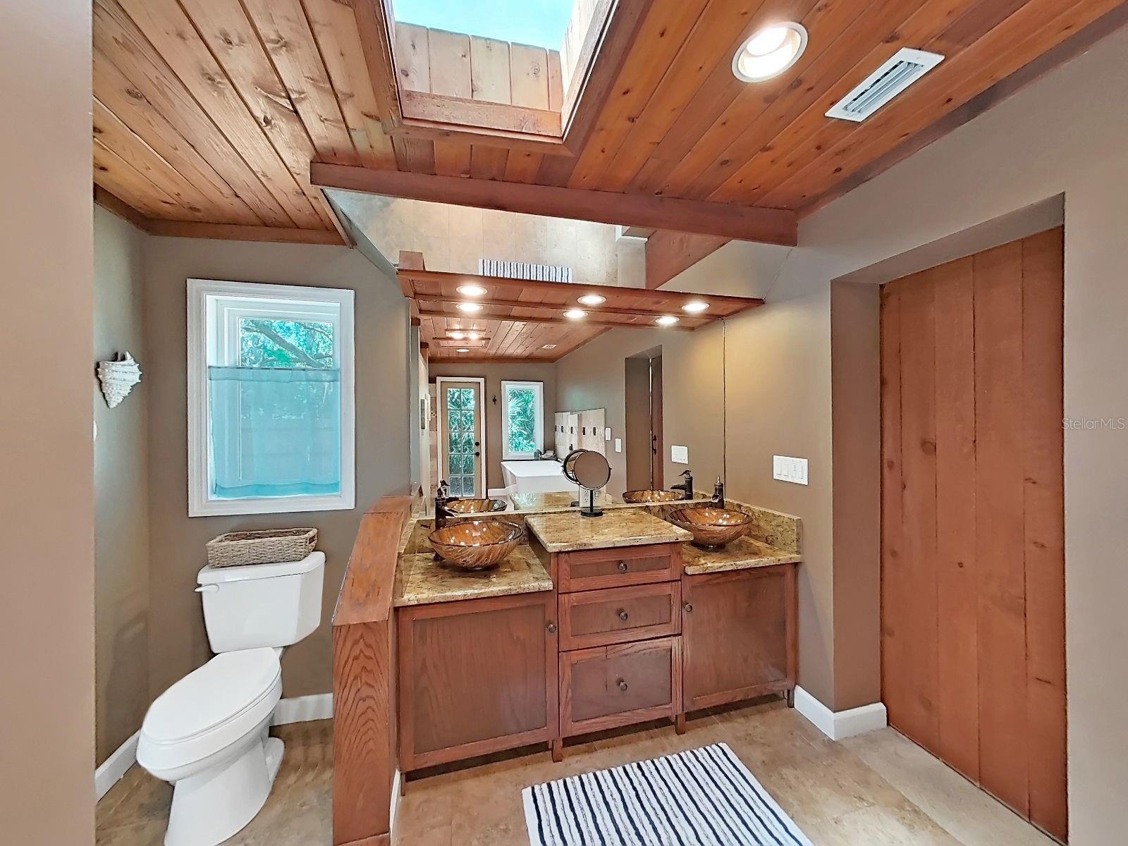 Primary bath with dual vessel sinks, granite counters, wood-planked ceiling with skylight & barn door. Elegance!
