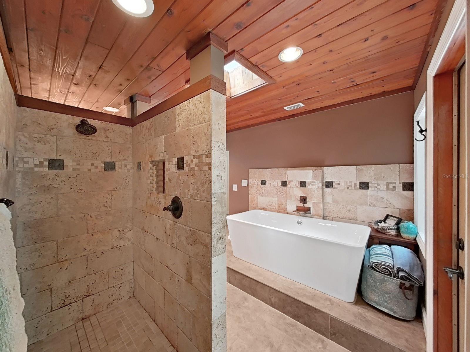 Luxurious primary bath with walk-in travertine shower. Notice the modern convenience of the shower control handle at the entrance (instead of underneath the shower head).