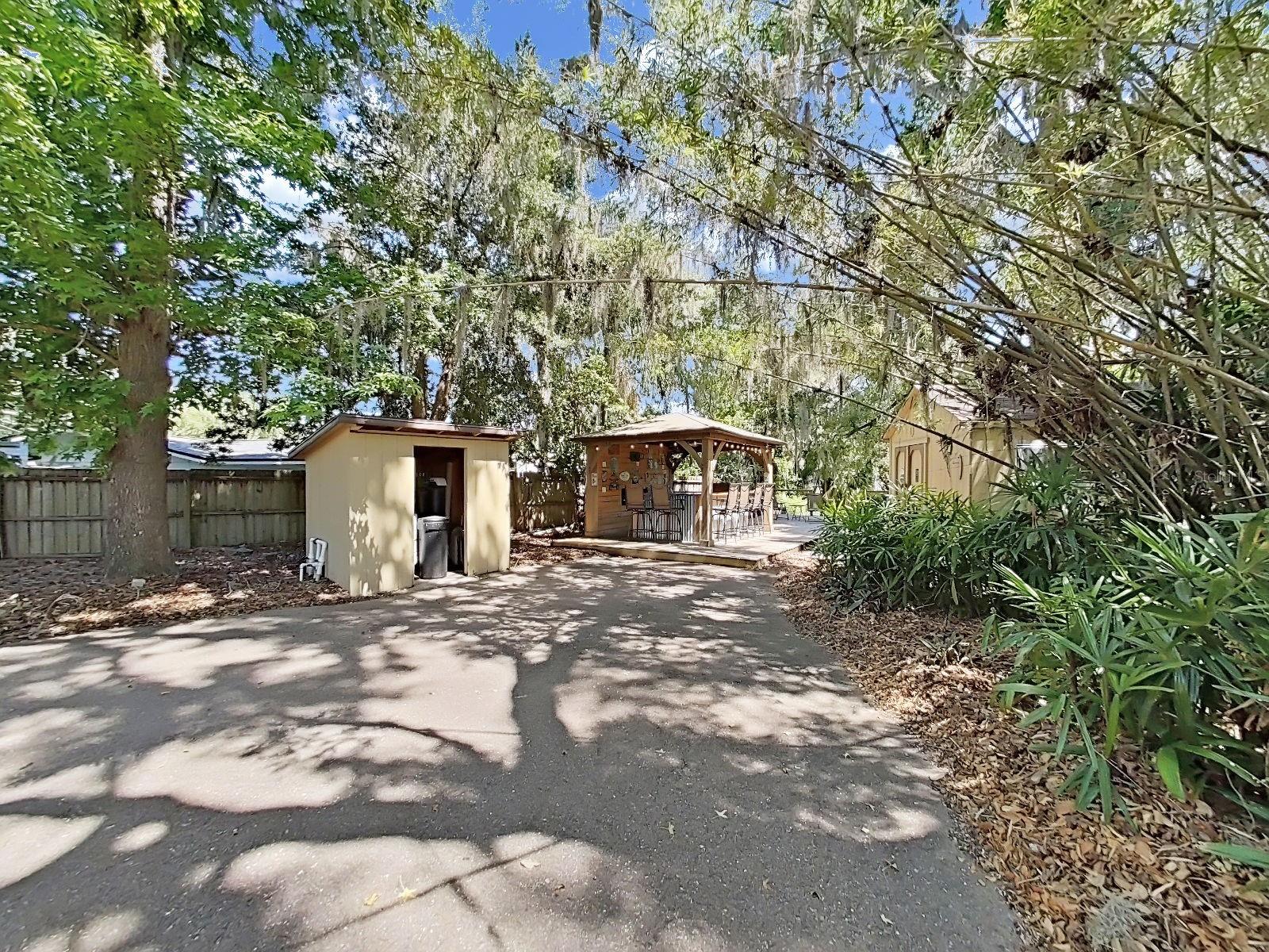 Spacious backyard view and sprawling paved path all nestled beneath a gorgeous canopy of mature trees and lush tropical landscape.