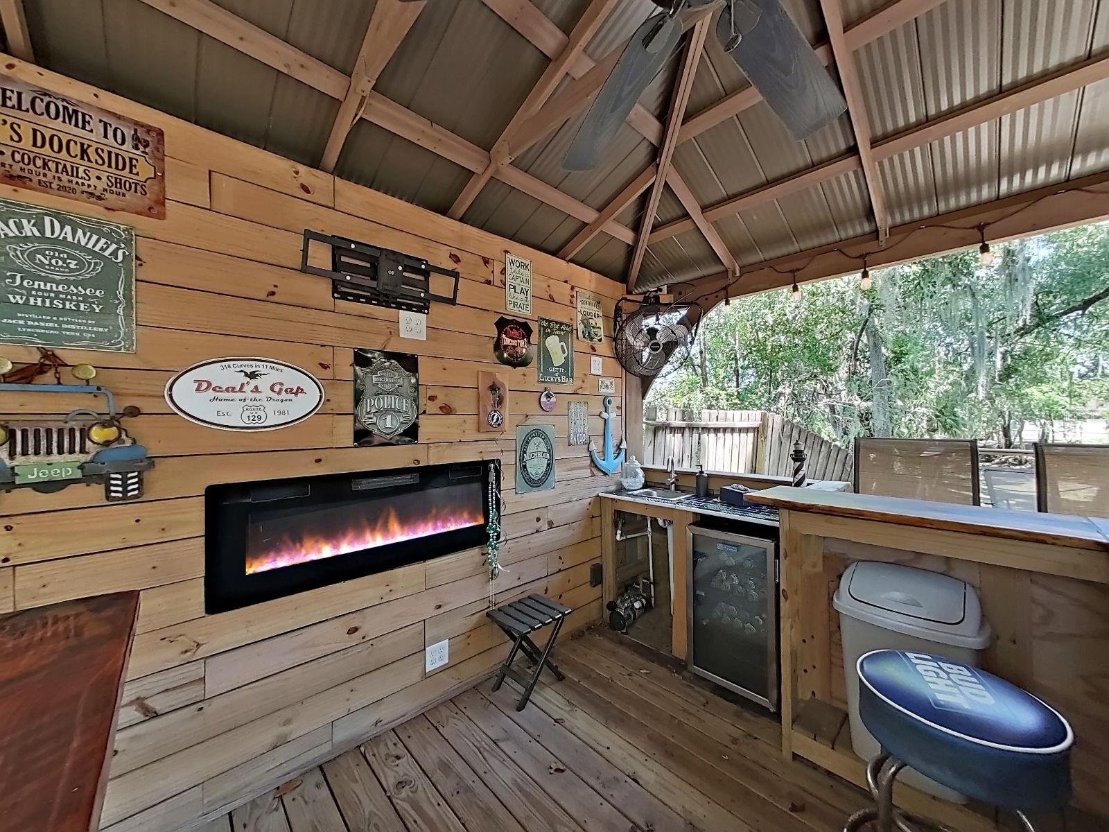 Fun-filled outdoor bar pavilion with a linear electric fireplace, beverage fridge & bar sink, wood planked walls, and mister fan- the ultimate backyard hangout!