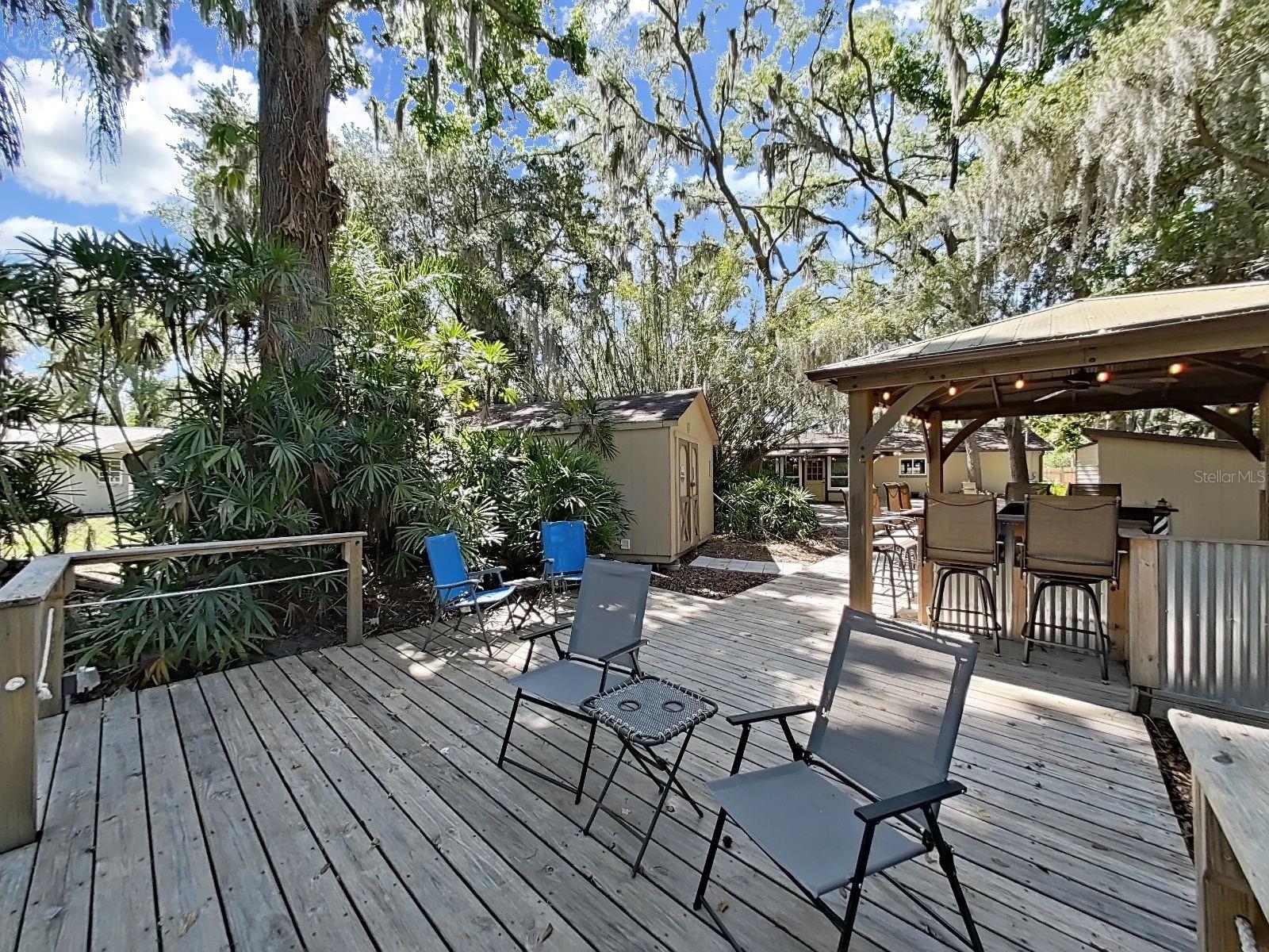 Spacious deck with seating area, flowing directly to the outdoor bar gazebo, insulated & climate-controlled storage shed, & lush landscaping. The backyard lifestyle is truly next level here!