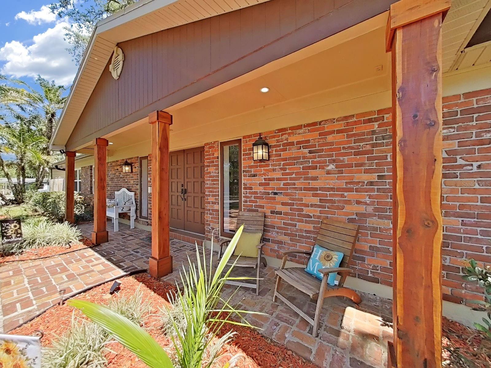 Inviting covered front porch with warm wood beam columns, brick accents, & cozy seating. The perfect spot to relax and enjoy the Florida breeze. Outdoor outlets/plugs on this porch are super convenient!