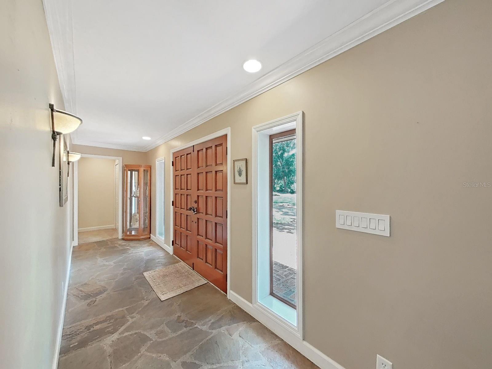 Grand foyer entry with stunning wood double doors, unique slate flooring, crown molding, & welcoming hallway. A truly impressive first step inside!