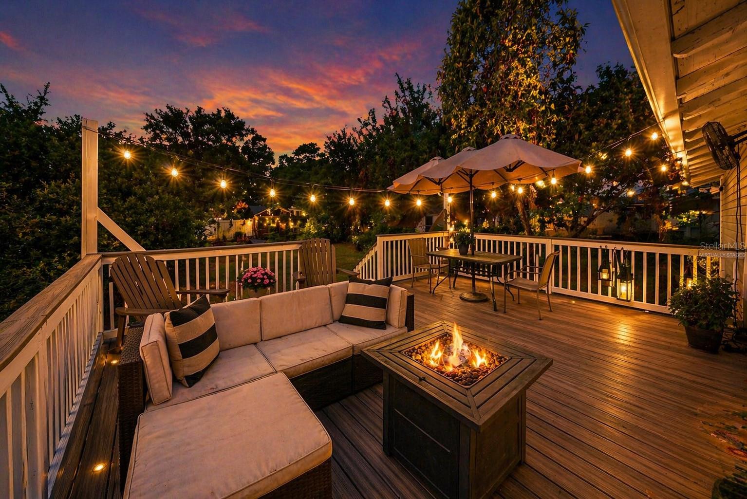 Virtually staged. Back deck at dusk with string lighting and fire feature, ideal for relaxing or entertaining.