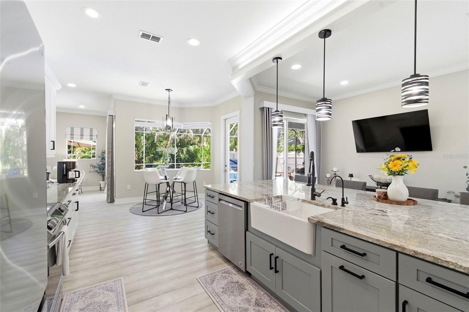 Stunning open-concept kitchen designed for both everyday living and entertaining, featuring a large center island with farmhouse sink, granite countertops, and ample cabinetry. Modern pendant lighting, stainless steel appliances, and sleek finishes create a clean, contemporary look. The space flows seamlessly into a bright dining area with large windows overlooking the pool and lush landscaping, while sliding glass doors provide easy indoor-outdoor living.