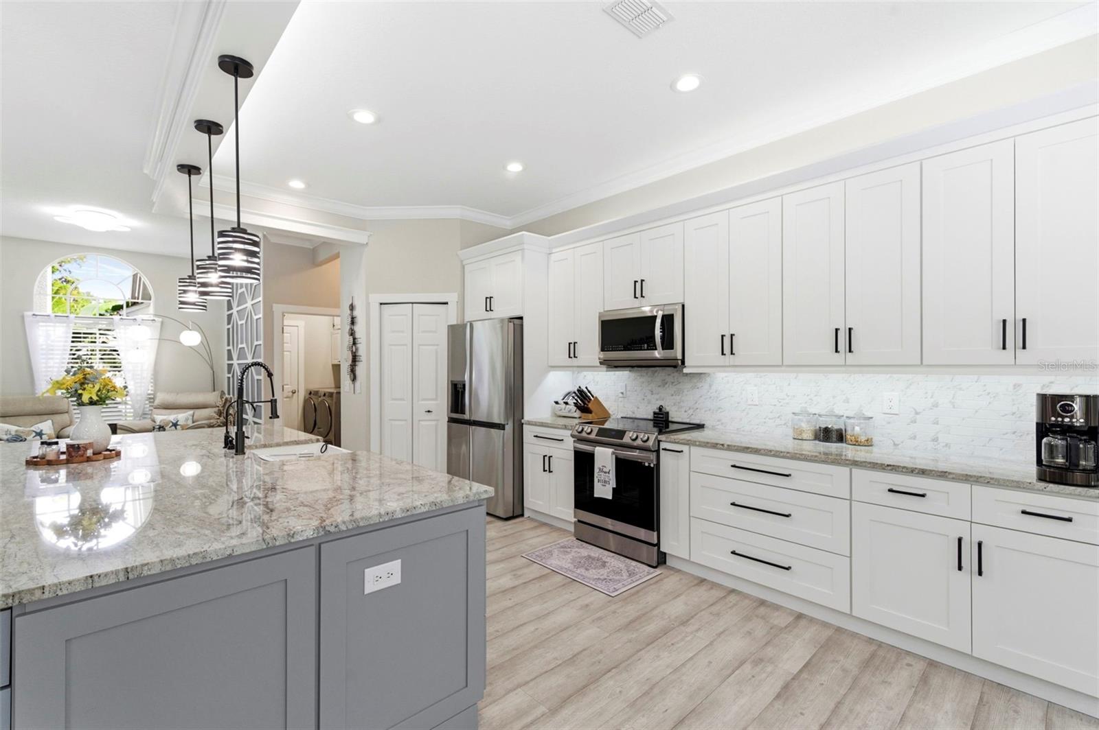 Stunning open-concept kitchen designed for both everyday living and entertaining, featuring a large center island with farmhouse sink, granite countertops, and ample cabinetry. Modern pendant lighting, stainless steel appliances, and sleek finishes create a clean, contemporary look. The space flows seamlessly into a bright dining area with large windows overlooking the pool and lush landscaping, while sliding glass doors provide easy indoor-outdoor living.