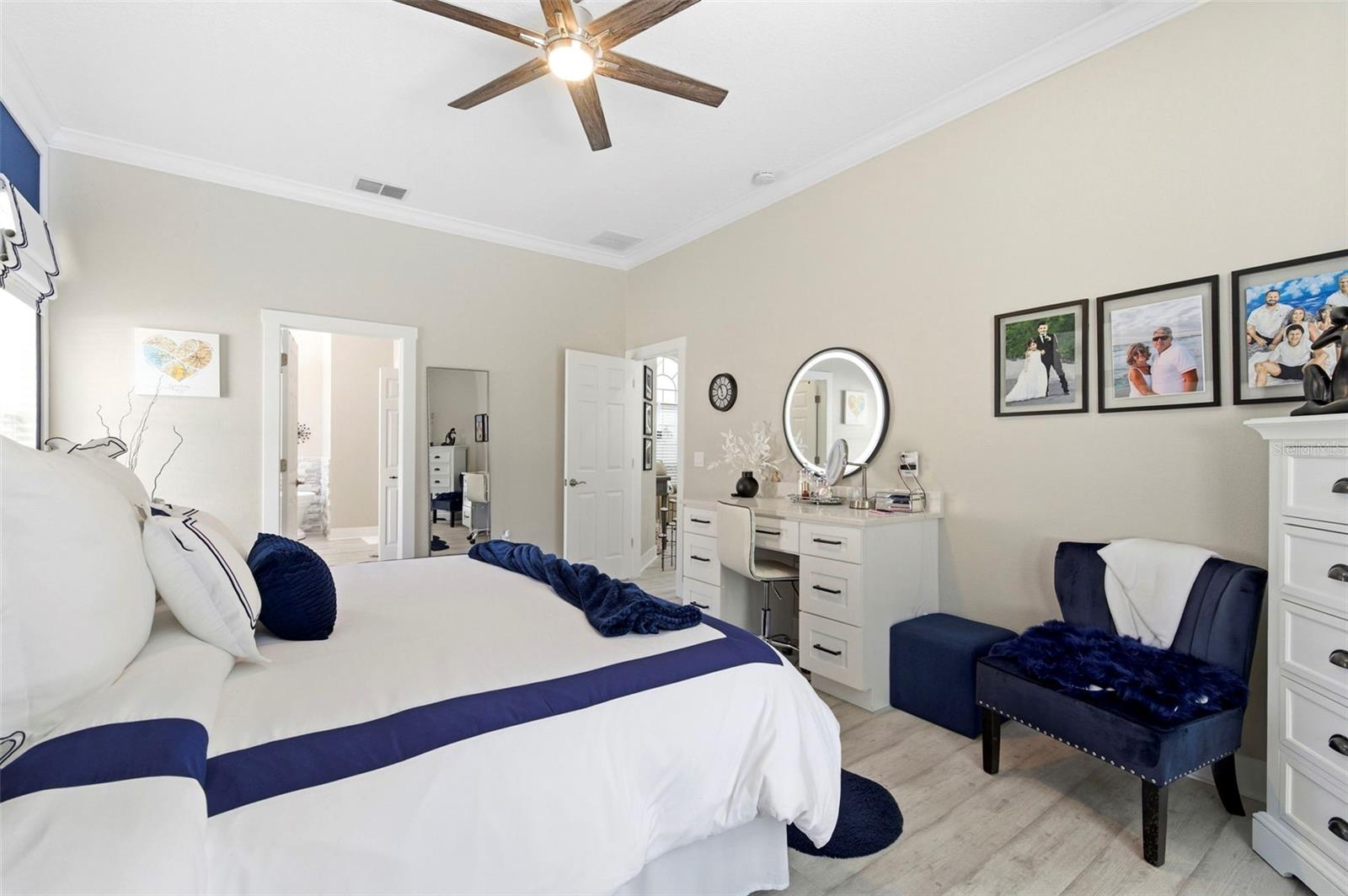 Stylish and serene primary bedroom featuring a striking accent wall with custom molding and designer finishes. The space offers a plush upholstered bed, coordinated décor, and a calming color palette that creates a true retreat. High ceilings and natural light enhance the open, airy feel, while the en-suite bathroom access adds convenience and functionality. A perfect blend of comfort and sophistication.