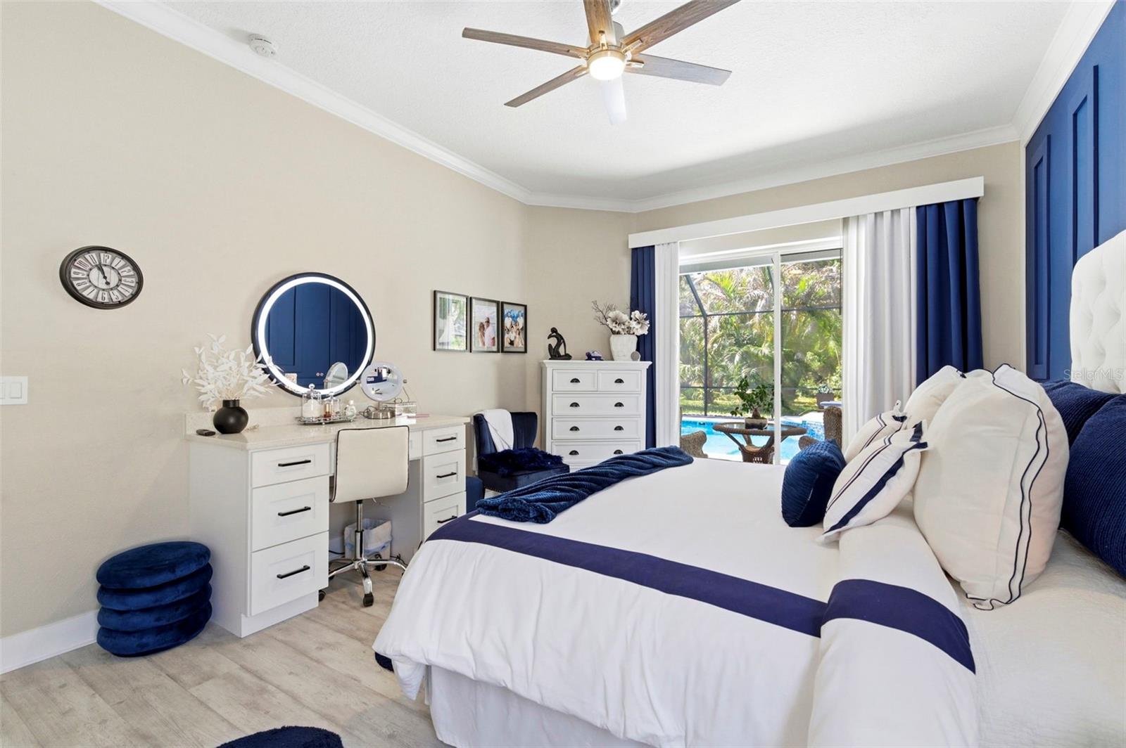 Bright and beautifully appointed bedroom featuring a serene color palette and stylish finishes throughout. Enjoy peaceful views of the pool and lush landscaping through large windows that fill the space with natural light. The room offers a comfortable layout with a dedicated vanity/desk area, ample storage, and modern fixtures, creating a perfect blend of functionality and relaxation.