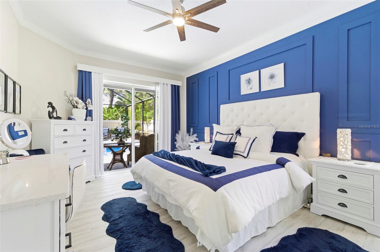 Bright and beautifully appointed bedroom featuring a serene color palette and stylish finishes throughout. Enjoy peaceful views of the pool and lush landscaping through large windows that fill the space with natural light. The room offers a comfortable layout with a dedicated vanity/desk area, ample storage, and modern fixtures, creating a perfect blend of functionality and relaxation.