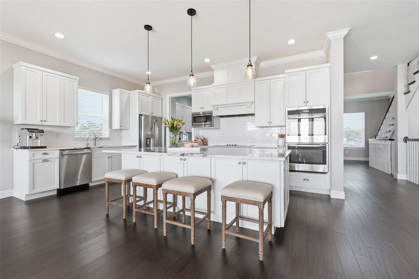 Kitchen features stainless steel appliances, a double oven, newer glass cooktop, and a huge center island with bar seating. The laundry room is to the back left, and elevator and stairs to the right.