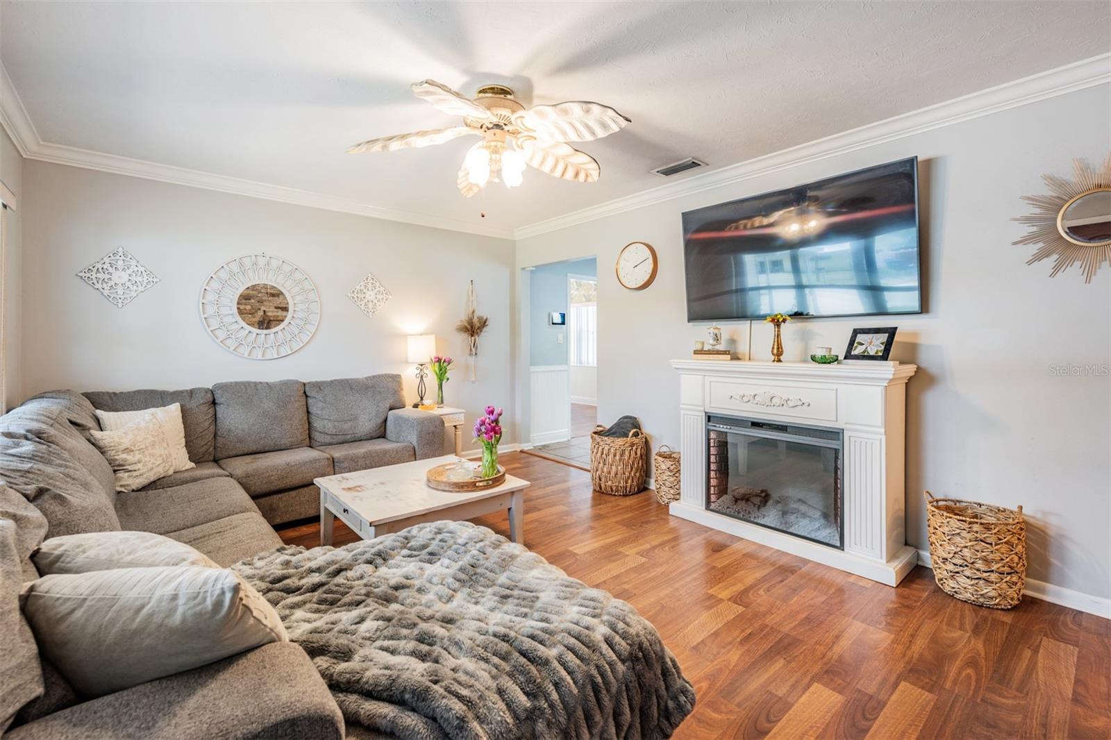 Main living area with decorative electric fireplace, crown molding and beautiful laminate wood look flooring