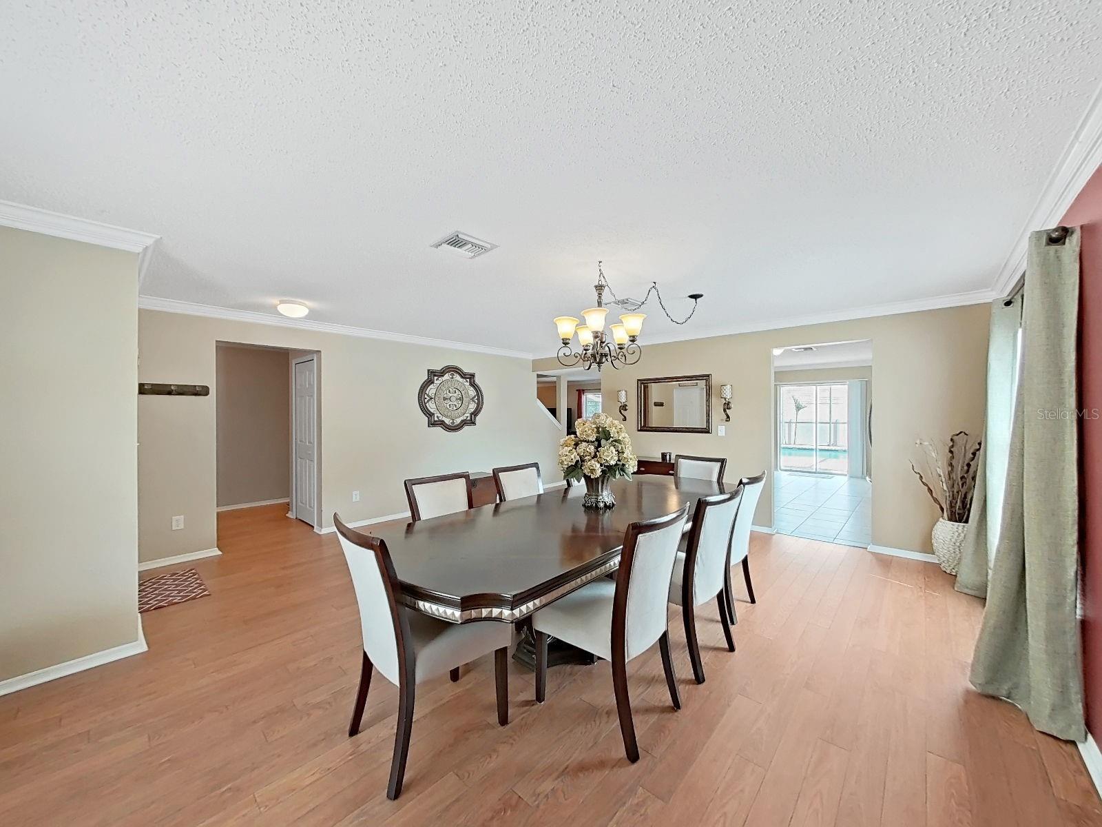 A grand dining room with warm floors, chandelier glow, and crown molding.