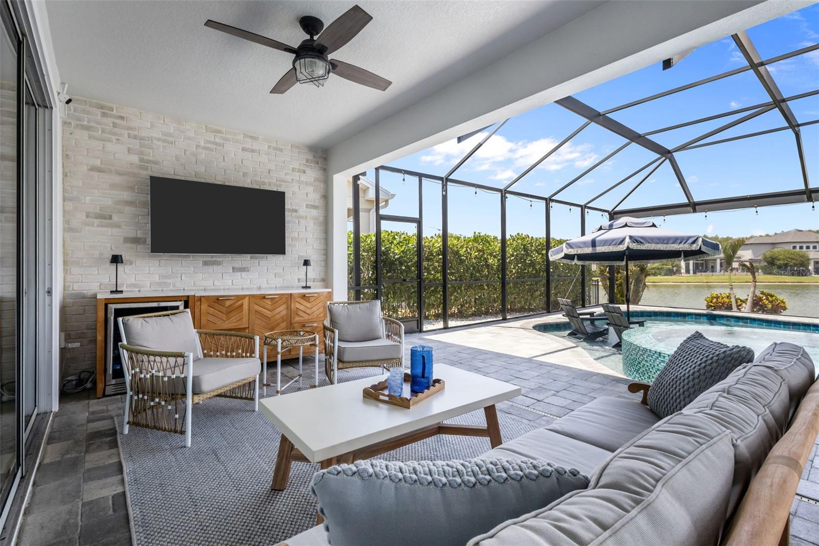 Screened lanai with covered seating area, brick accent wall, and space for dining and entertaining.