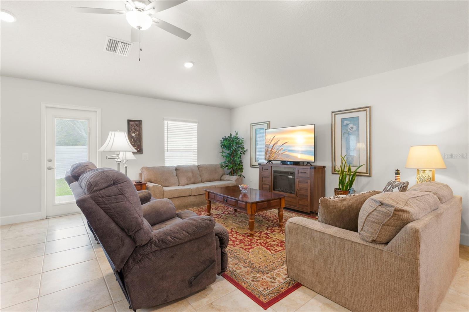 The spacious living room offers neutral tones, oversized tile flooring, recessed lighting, and a ceiling fan, with airy proportions and direct access to the rear patio for seamless indoor-outdoor flow.