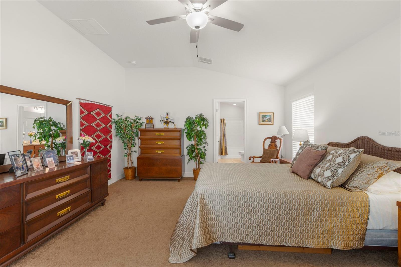 The generous primary bedroom features vaulted ceilings, a ceiling fan, neutral tones, and direct access to the ensuite bath.