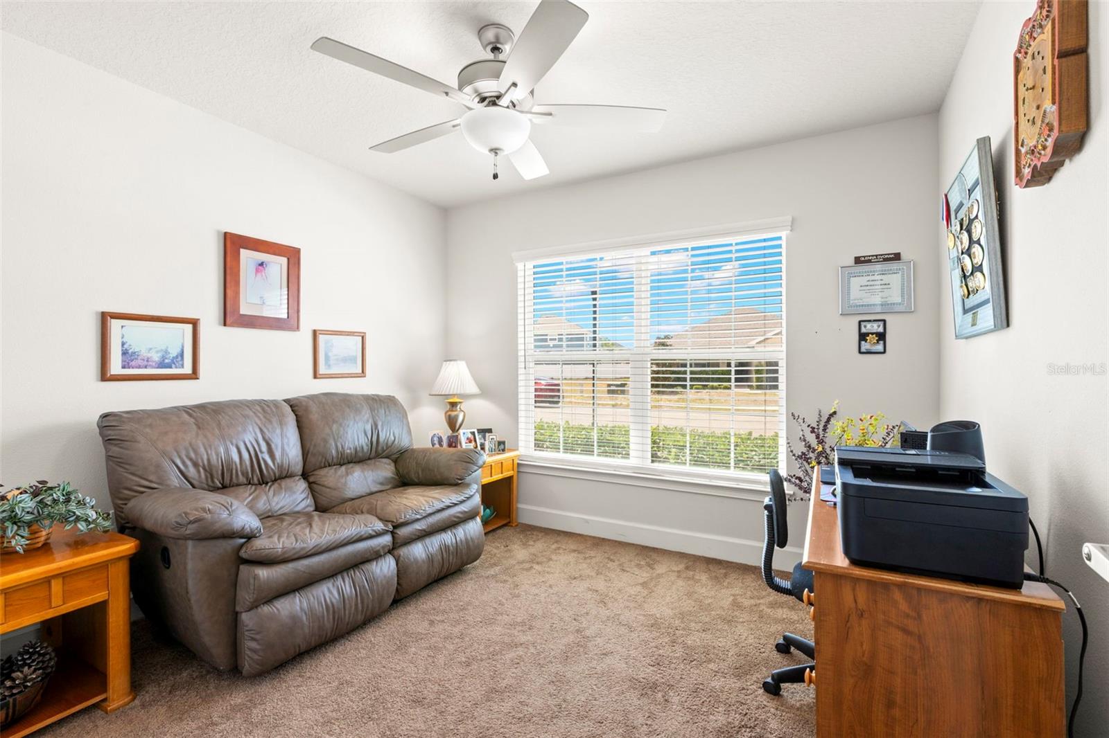 Bedroom 2 offers flexibility for guests, family, or a home office, featuring neutral finishes, plush carpeting, a ceiling fan, and a large front-facing window that brings in abundant natural light.