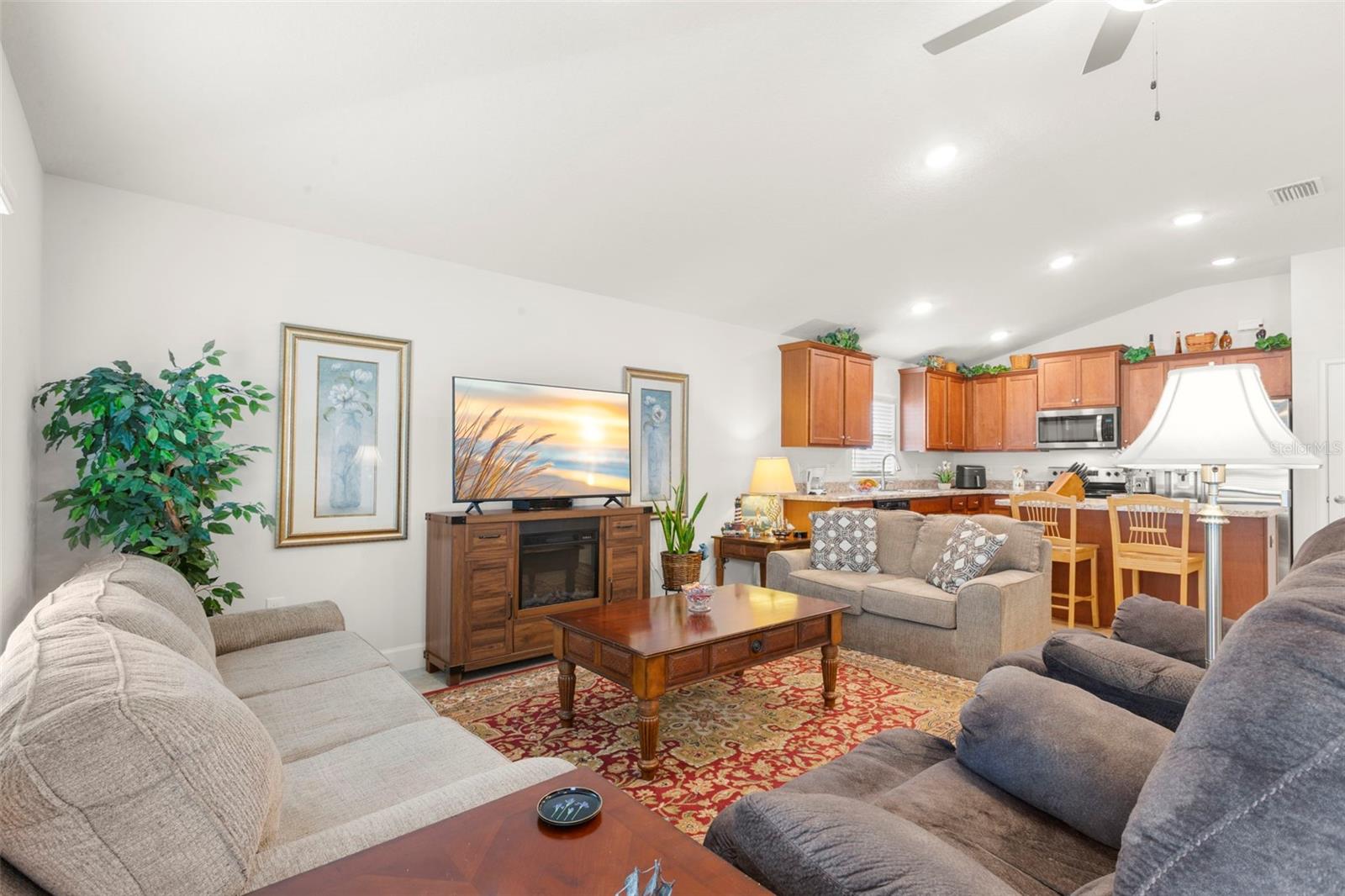 Open sightlines connect the living area to the kitchen, where warm wood cabinetry, recessed lighting, and bar seating create a functional and inviting central gathering space.