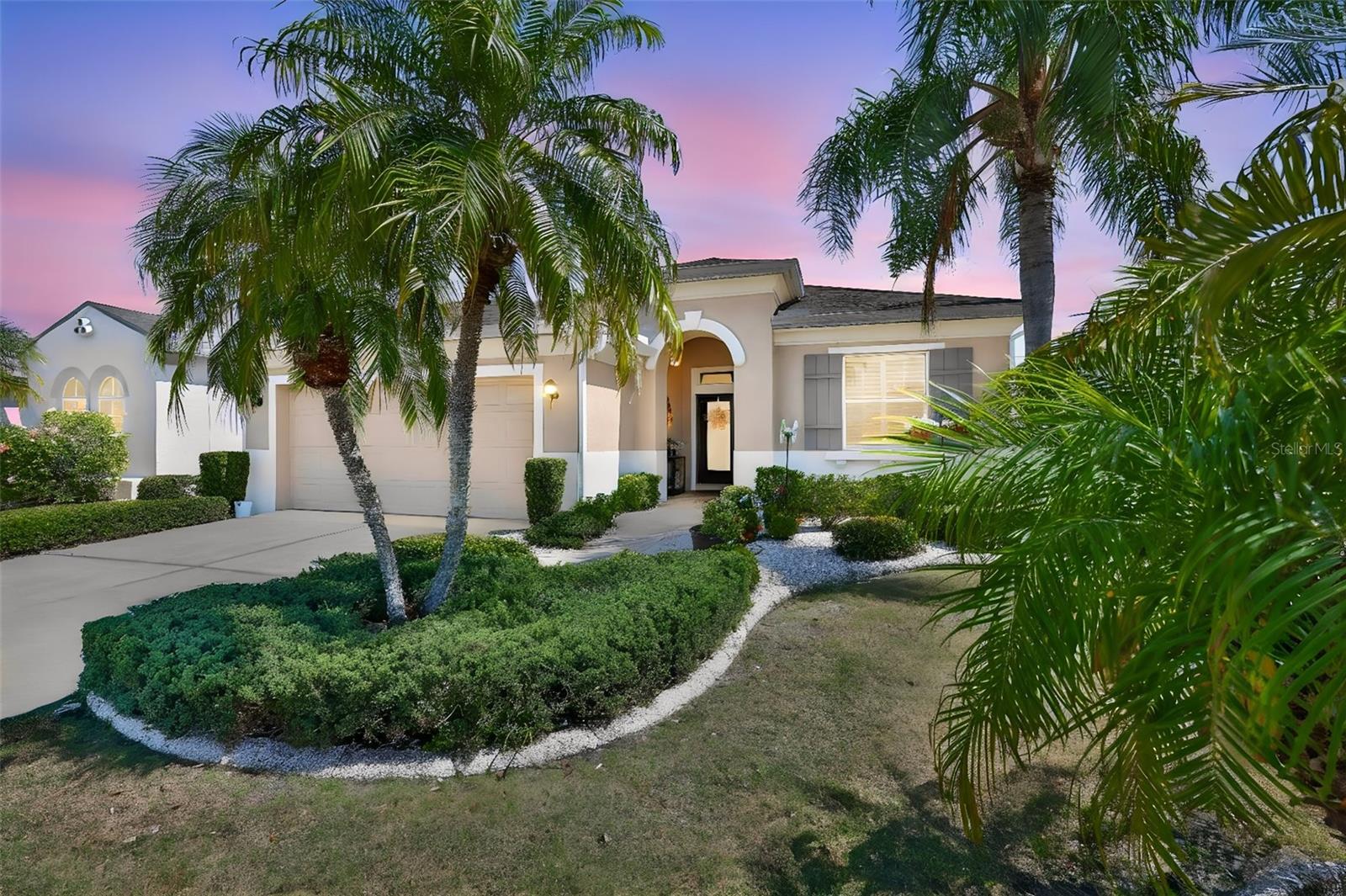 Exquisite home with swaying palm trees, landscape curbing and a large, arched entryway.