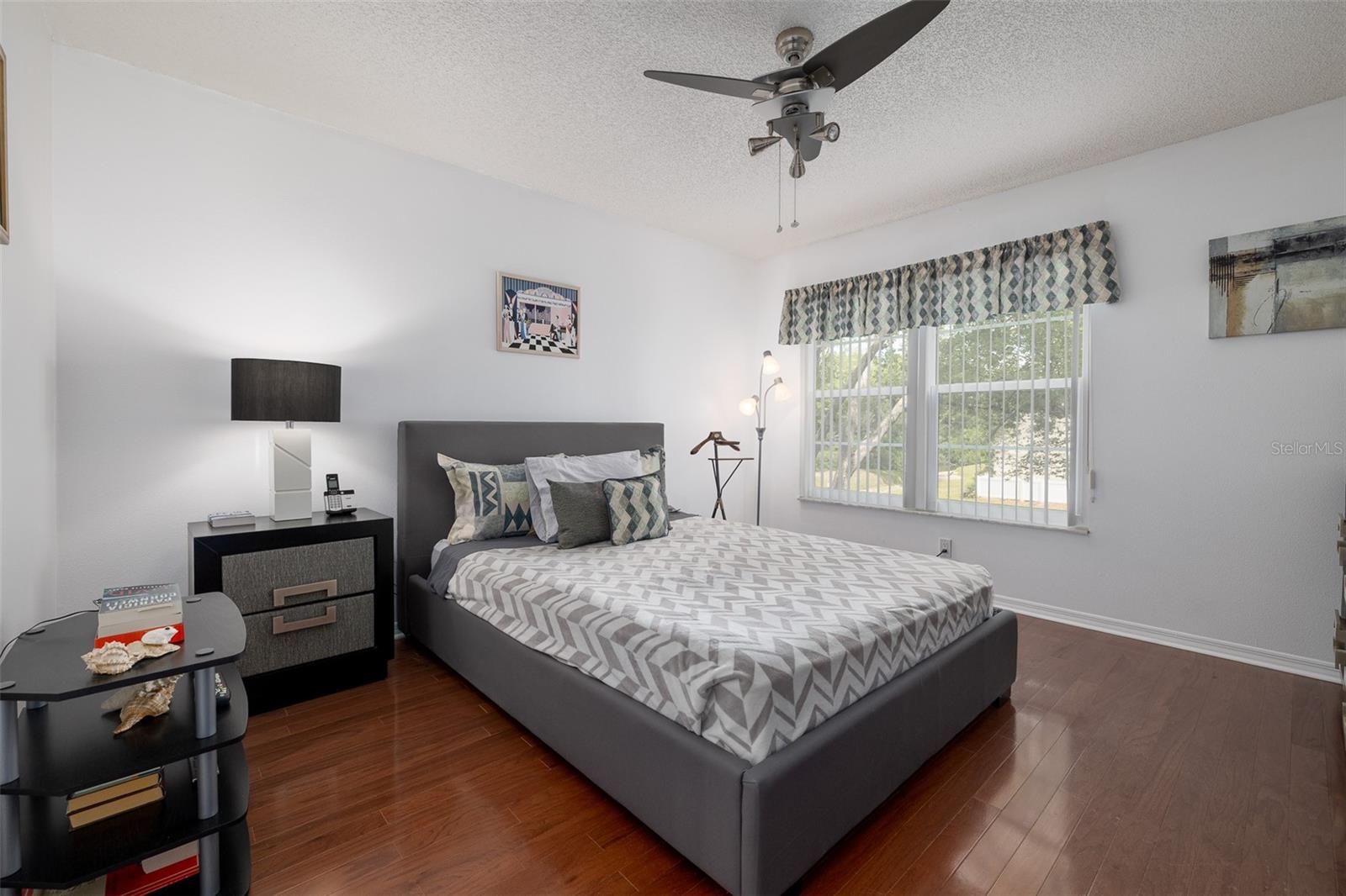 Owner's bedroom, wood flooring, ceiling fan, overlooking trees, landscaping, and water