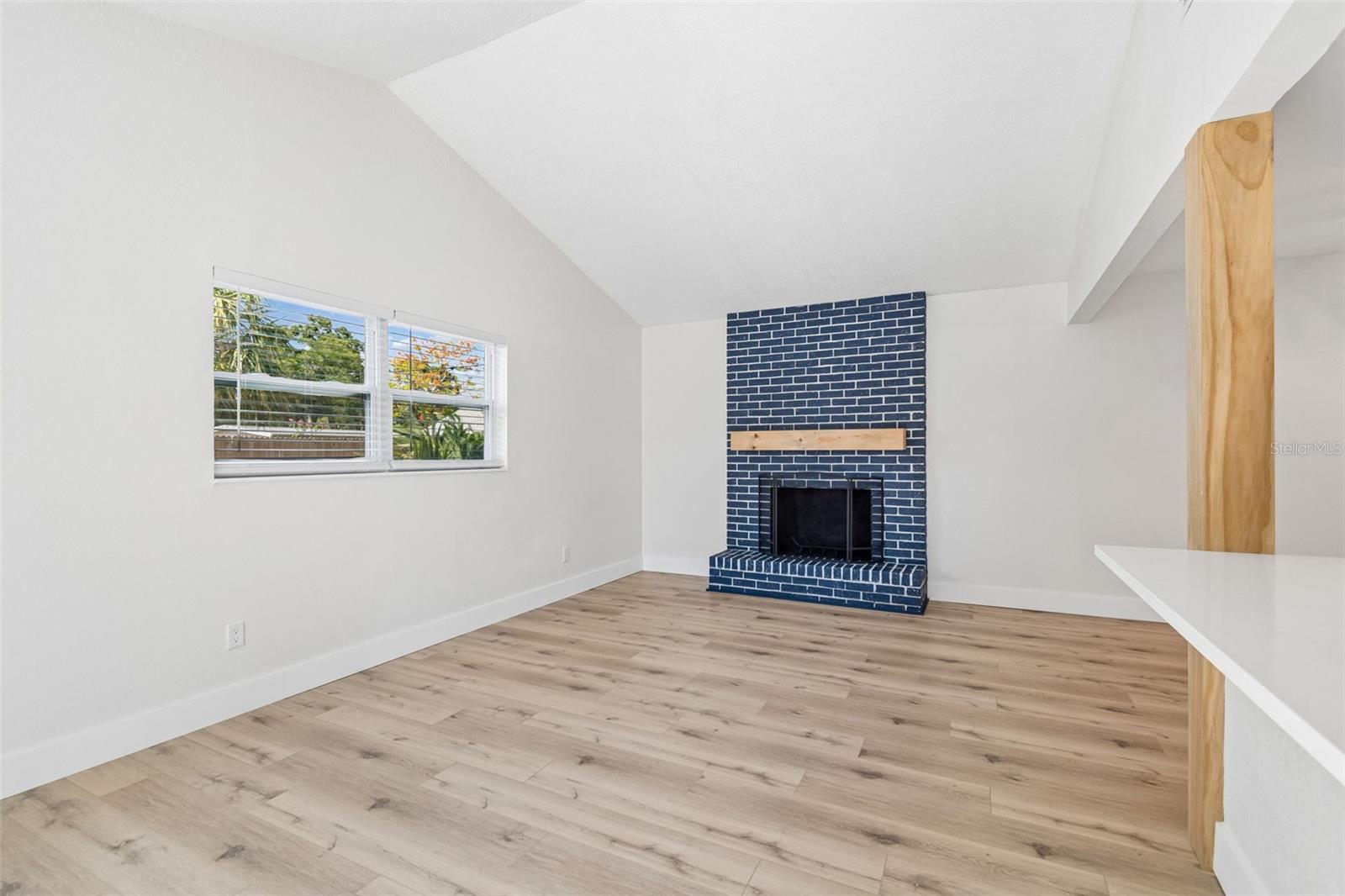 Living room with vaulted ceilings and brick wood burning fireplace.
