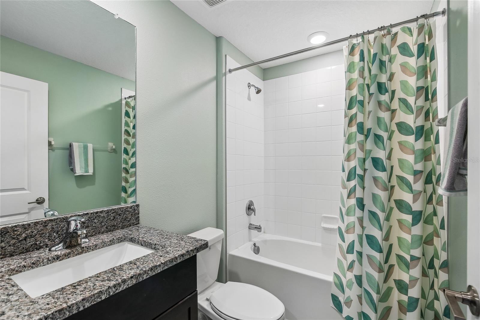 Secondary BathroomSecondary bathroom with a single undermount sink, espresso cabinetry, granite countertop, and a tub/shower combination with white tile surround. Tile flooring and recessed lighting.