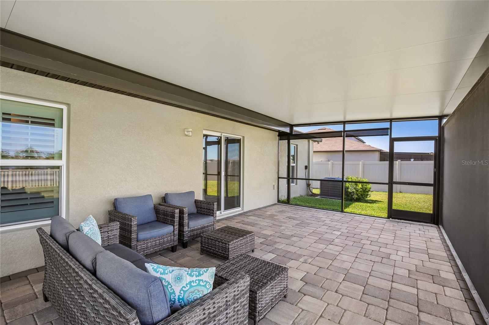 Screened lanai with pavered flooring and a solid insulated roof panel. Sliding glass door provides access from the interior; enclosure includes a screen door to the rear yard.