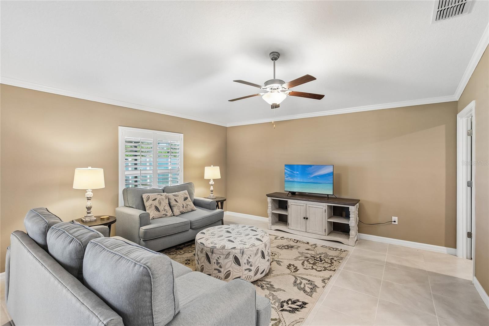 Open-concept living area with tile flooring, crown molding, and a ceiling fan, opening directly to a kitchen with dark cabinetry, granite countertops, a breakfast bar, and stainless steel appliances.