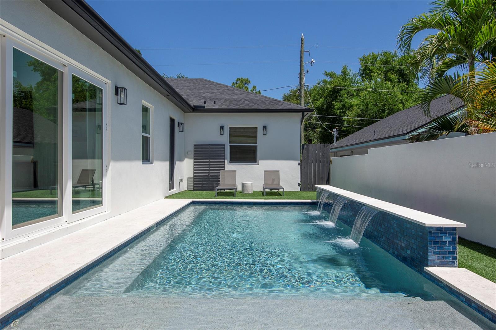 The resort-style backyard serves as a natural extension of the home, featuring a pool with waterfall and sun shelf, expansive paver patios, a covered lounge area, and built-in media capability for elevated outdoor entertaining.