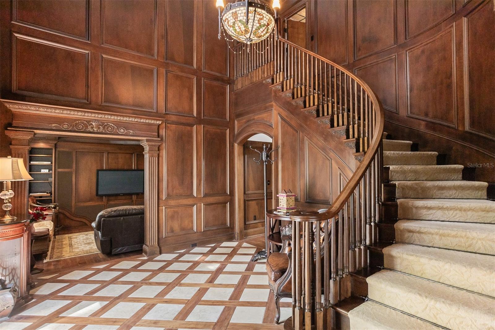 The entryway features a striking staircase descending gracefully and beyond it you get a view into the cozy, well-appointed sitting room