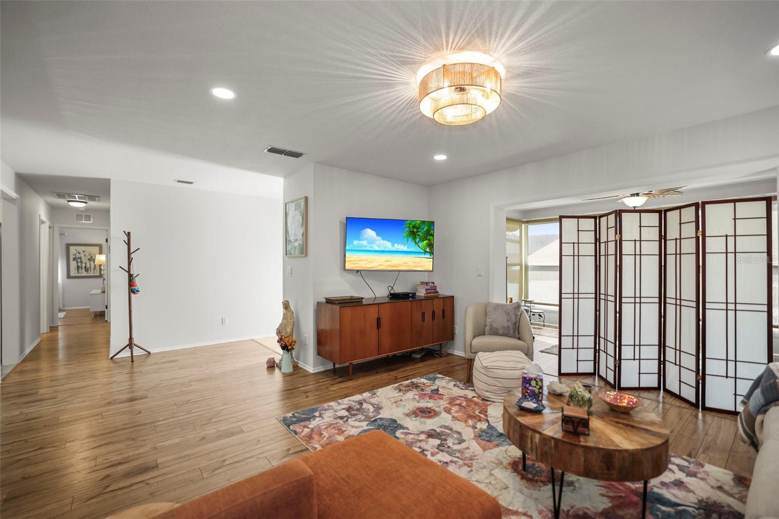 Living room with view towards bedrooms and front door with enclosed lanai to the right.