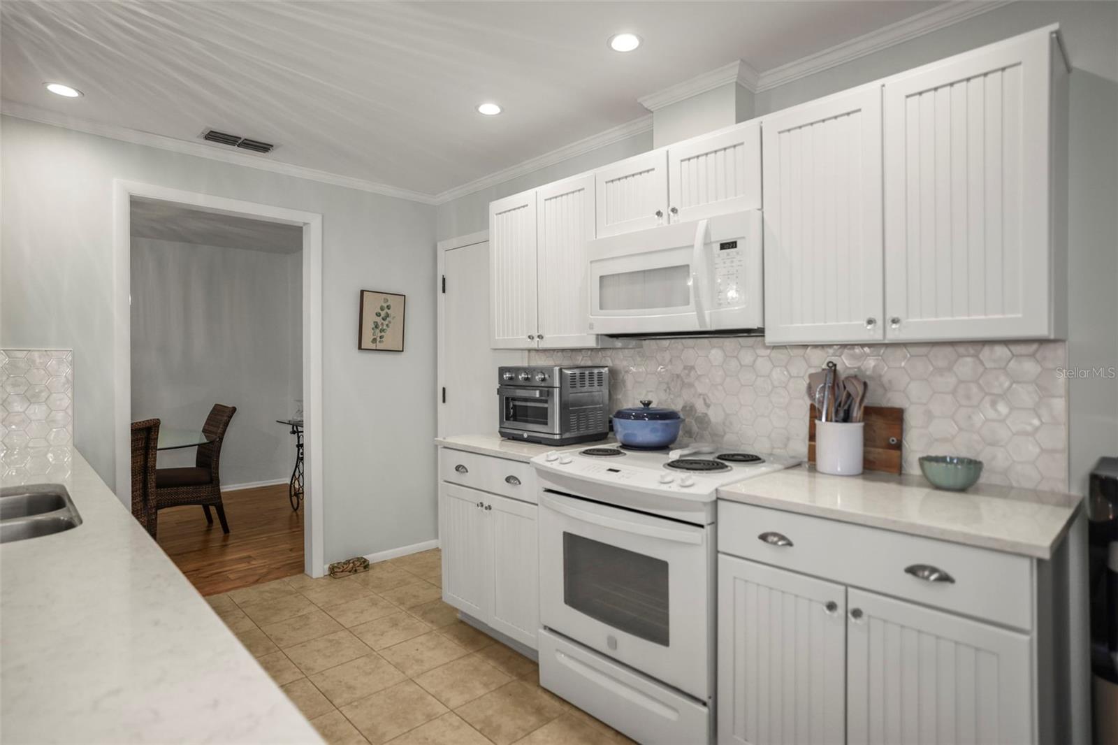 Kitchen with Solid surface counters, hardwood beadboard cabinetry, pretty glass tile backsplash, ceramic tile flooring and a pass through to the living room