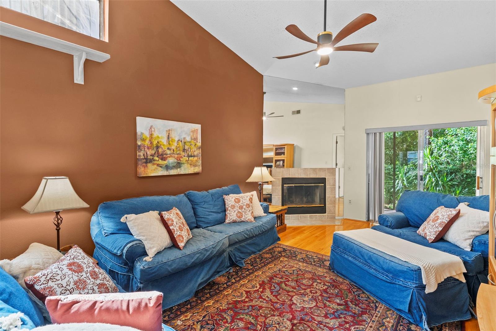 Inviting living space with soaring ceilings, ceiling fan, cozy fire place and warm accent wall.