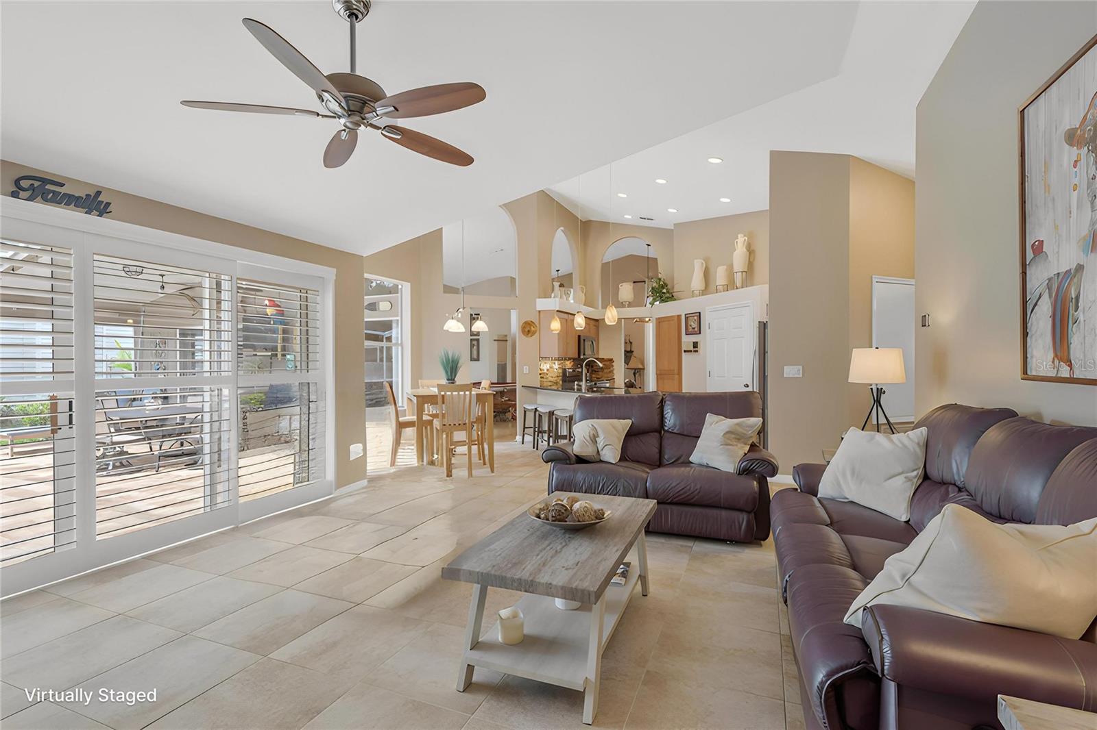 The open kitchen flows seamlessly into the family room, where abundant natural light pours through sliding glass doors accented with stylish Plantation Shutters.