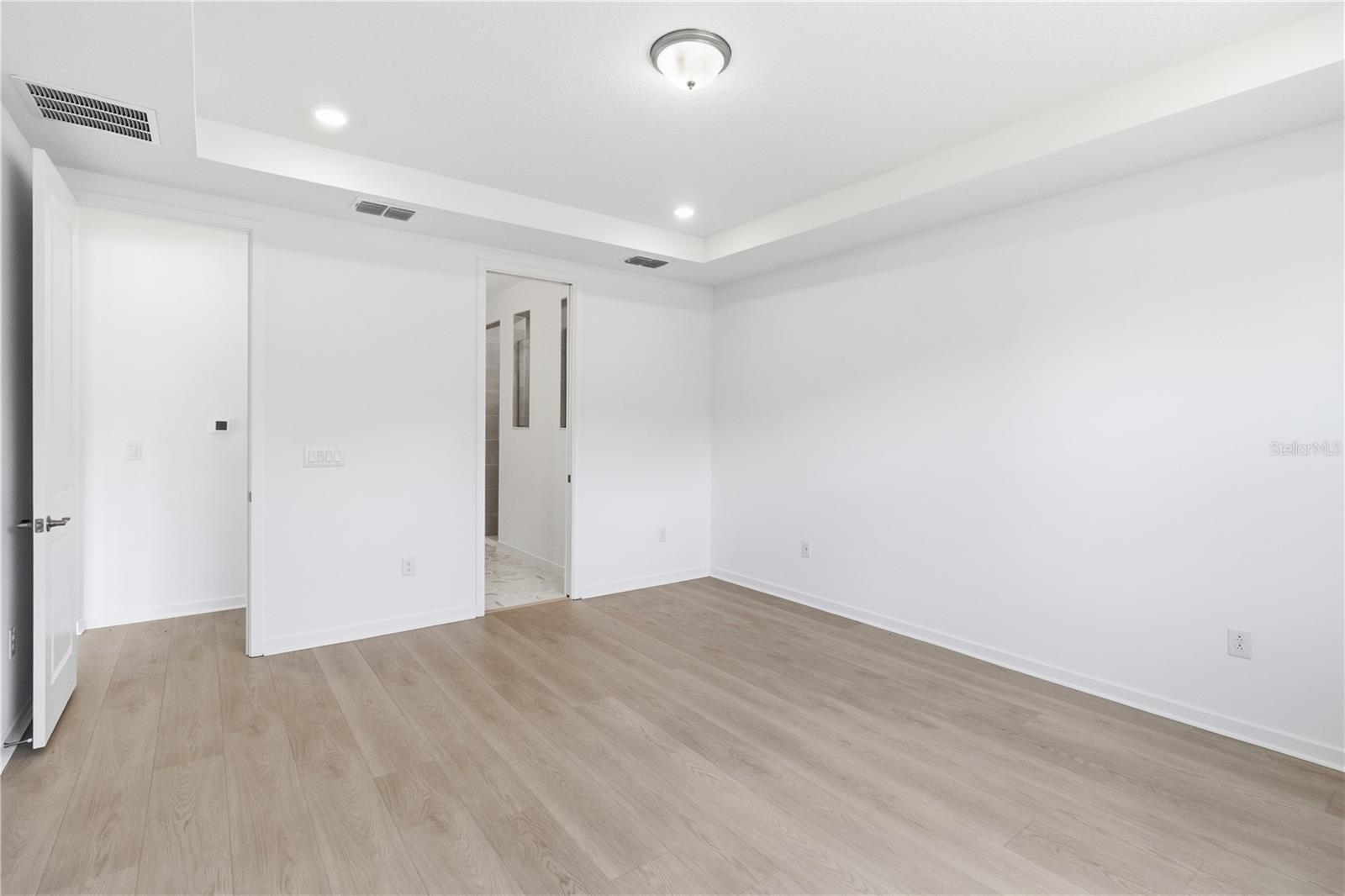 Spacious bedroom with warm flooring, bright walls, and flexible furniture options.