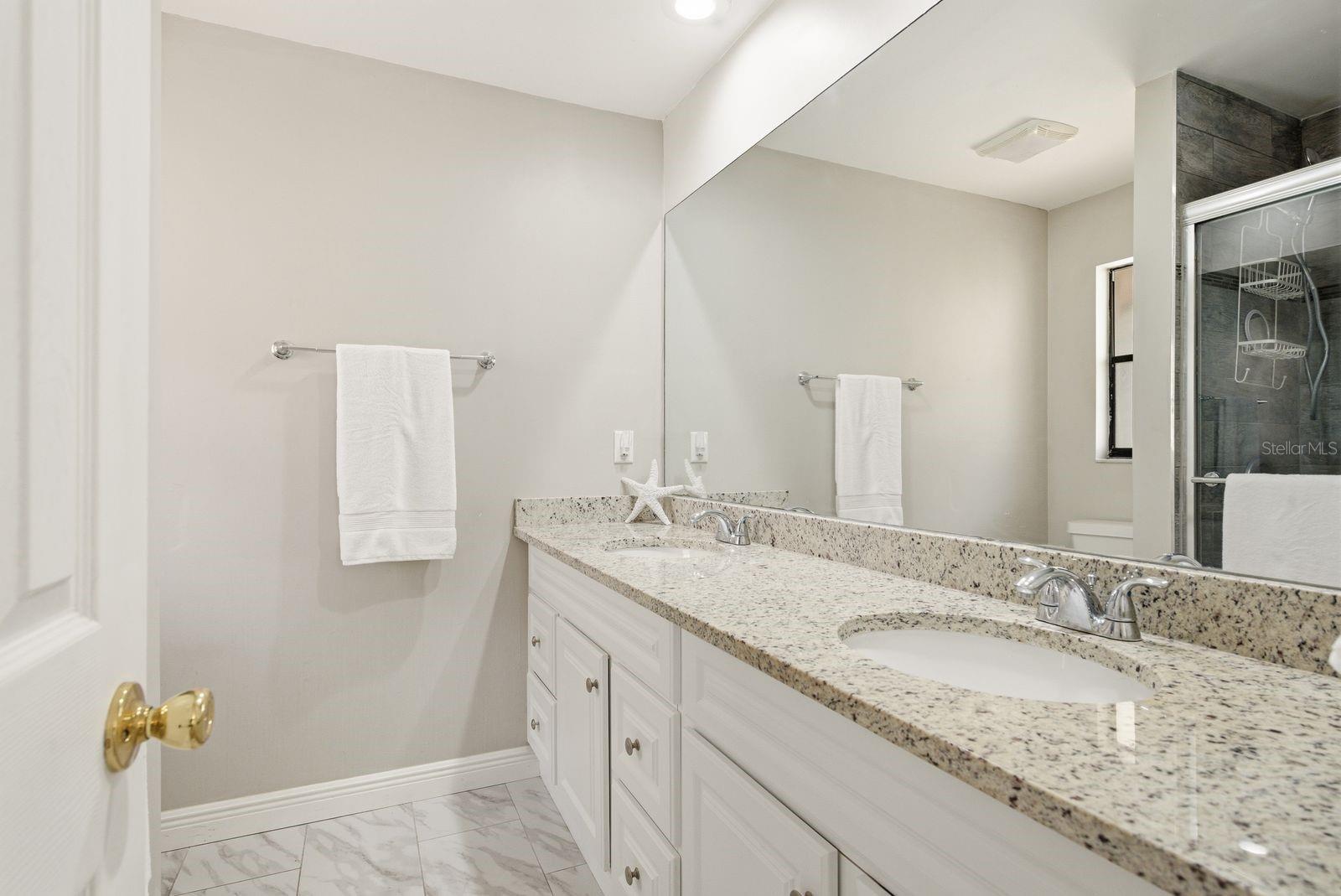 Primary bathroom with dual sinks, granite counters and a  step-in shower