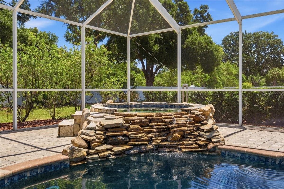 Exquisite custom rock waterfall spa featuring natural stone accents and a serene spillover effect into the sparkling pool below.