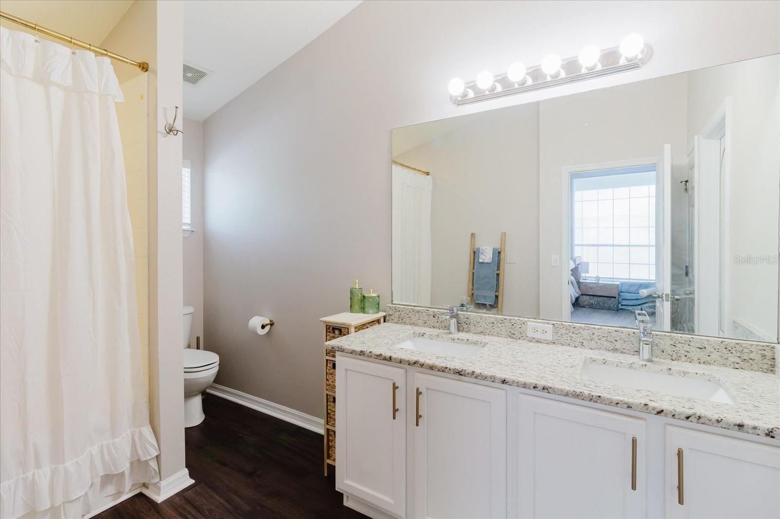 Primary Ensuite Bathroom With Luxury Vinyl Floors, Granite Double Vanity, and Shower With A Generous Soaking Tub